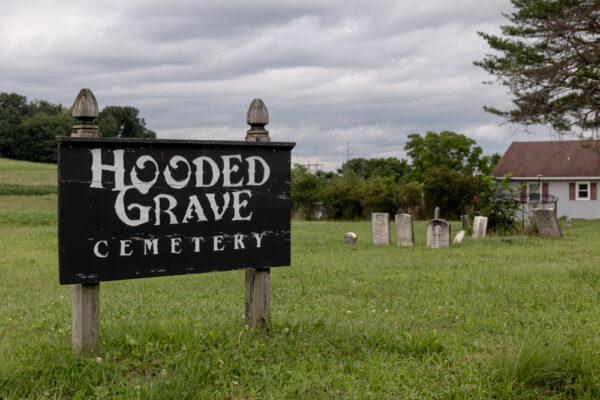 A sign for the Hooded Grave Cemetery in front of gravestones in Columbia County PA