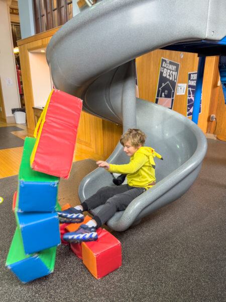 Boy going down the tornado slide and knocking over blocks at the Punxsutawney Weather Discovery Center