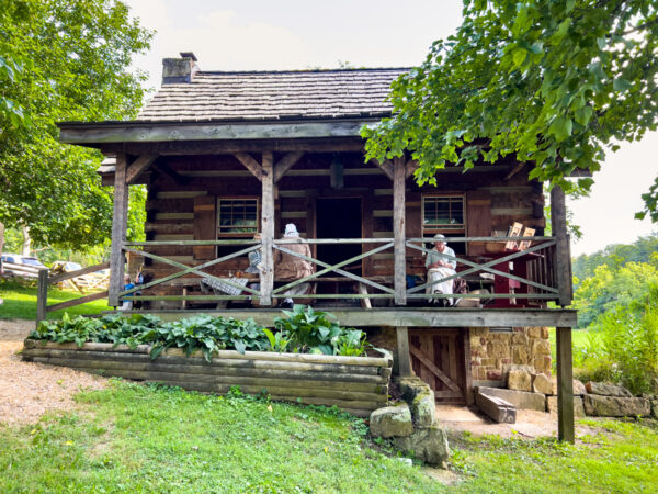 Women in colonial dress sit outside the log cabin at the Oliver Miller Homestead in Allegheny County PA