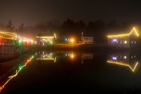 Decorated historic buildings reflecting in water during Holiday Lights at Gring's Mill in Reading Pennsylvania