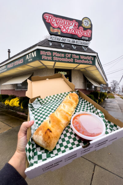 Man holding a Romano's stromboli outside of the Philadelphia area restaurant on a cloudy day.