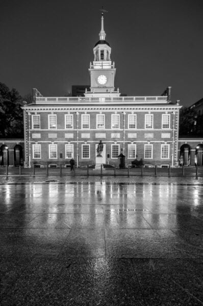 A black and white photo of Independence Hall in Philadelphia with it's reflection in the wet ground below