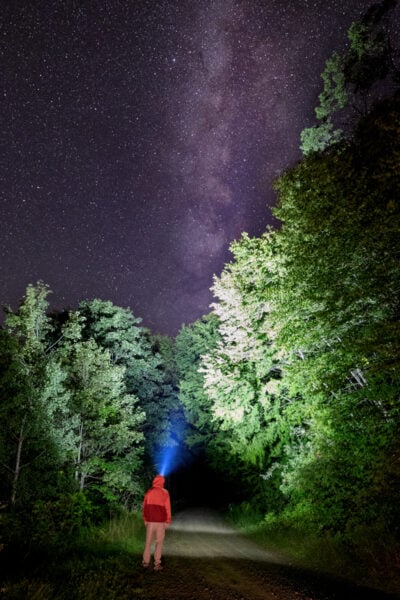 Man with a light on a forested road in Suquehannock State Forest below the Milky Way